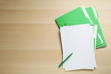 Light green files with blank sheets of paper and pen on wooden table, flat lay. Space for text