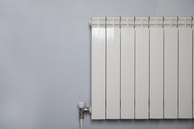 Modern heating radiator on light wall indoors, space for text