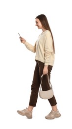 Photo of Young woman in casual outfit using smartphone while walking on white background