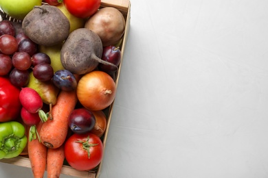 Wooden crate full of harvested vegetables and fruits on light table, top view. Space for text