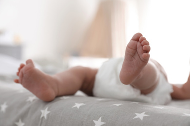 Cute little baby in diaper lying on bed in room, closeup