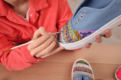 Woman painting on sneaker at wooden table, closeup. Customized shoes