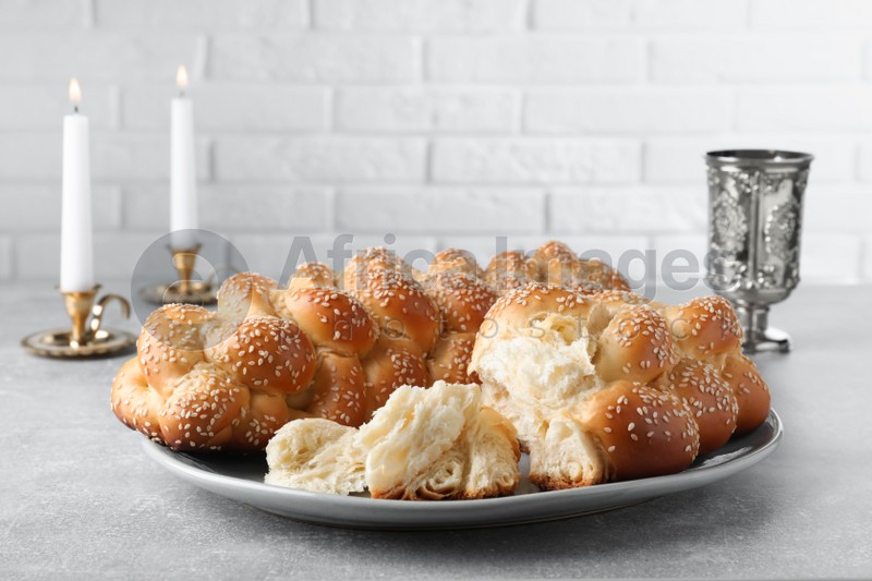Photo of Homemade braided bread with sesame seeds, goblet and candles on grey table. Traditional Shabbat challah