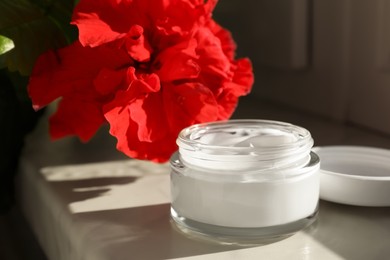 Photo of Jar of face cream and flower on white table indoors