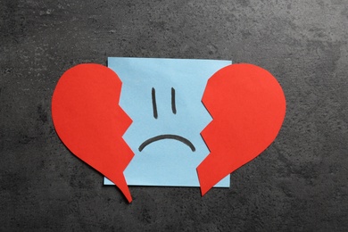 Sticker with sad face and broken heart on grey background, flat lay