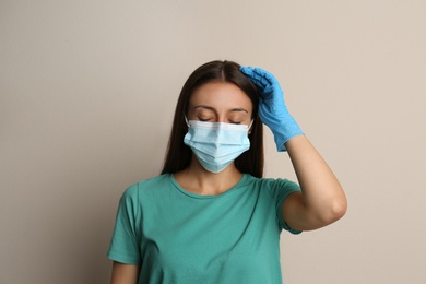 Stressed woman in protective mask on beige background. Mental health problems during COVID-19 pandemic