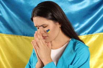Photo of Sad young woman with clasped hands near Ukrainian flag