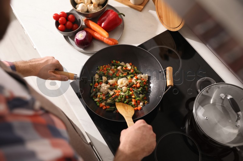 Man stirring mix of fresh vegetables in frying pan, above view