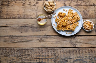 Photo of Delicious peanut kozinaki bars, nuts and honey on wooden table, flat lay. Space for text