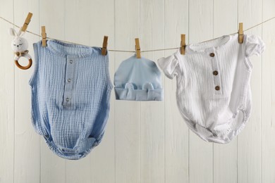 Baby clothes and accessories hanging on washing line near white wooden wall