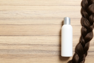 Photo of Shampoo bottle and braid on wooden background, flat lay. Space for text