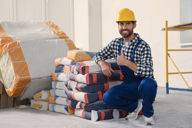 Professional builder in uniform near cement bags indoors