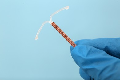 Doctor holding T-shaped intrauterine birth control device on light blue background, closeup