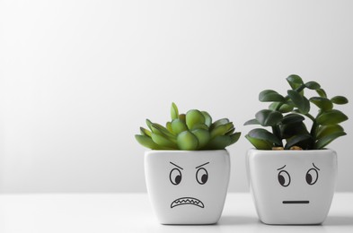 Photo of Beautiful potted houseplants with angry and concerned faces on white table, space for text. Emotional management