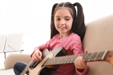 Little girl playing guitar at home. Learning music notes