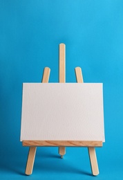 Wooden easel with blank canvas board on color background. Children's painting