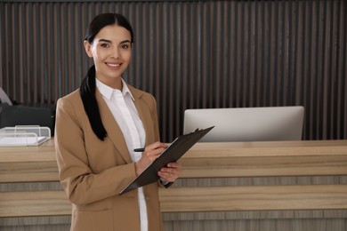 Receptionist with clipboard near countertop in office, space for text