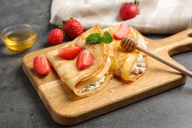 Photo of Delicious thin pancakes with strawberries, cottage cheese and honey on grey table