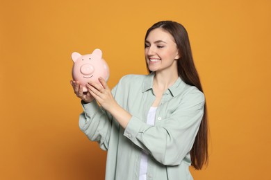 Photo of Happy young woman with piggy bank on orange background