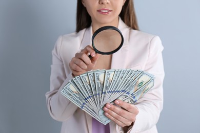 Photo of Expert authenticating 100 dollar banknotes with magnifying glass on light grey background, closeup. Fake money concept