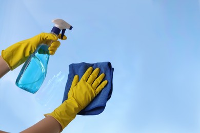 Woman cleaning window glass with rag and detergent, closeup. Space for text
