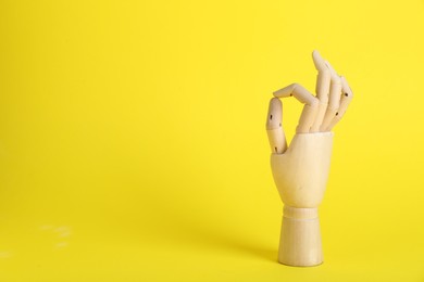 Photo of Wooden mannequin hand showing okay gesture on yellow background. Space for text
