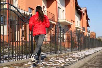 Woman running along street on winter day, back view. Outdoors sports exercises