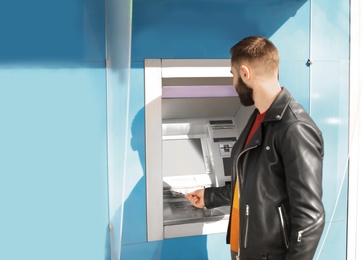 Young man taking money from cash machine outdoors