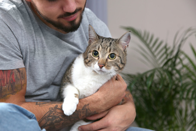 Man with tabby cat near window indoors, closeup. Friendly pet