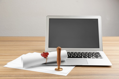 Notary's public pen and sealed document near laptop on wooden table