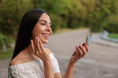 Photo of Beautiful young woman looking at herself in cosmetic pocket mirror outdoors
