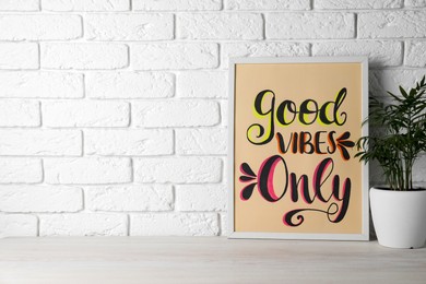 Board with phrase Good Vibes Only and houseplant on wooden table near white brick wall, space for text