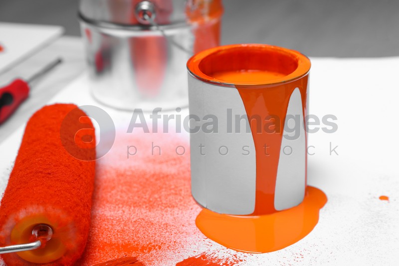 Cans of orange paint and roller on white table indoors