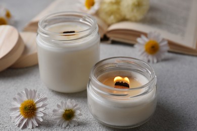Photo of Burning scented candles and chamomile flowers on light gray textured table, closeup