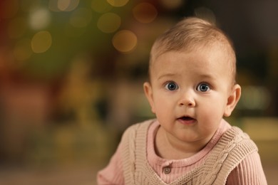 Photo of Cute little baby and blurred Christmas lights on background, space for text. Winter holiday