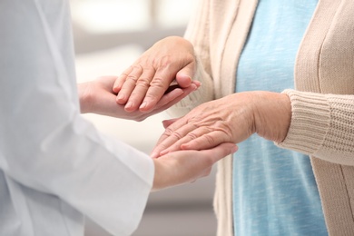 Nurse comforting elderly woman against blurred background, closeup. Assisting senior generation