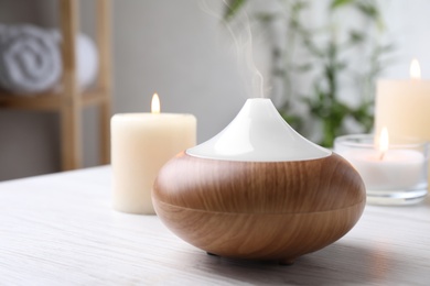 Aroma oil diffuser and burning candles on white wooden table indoors, space for text