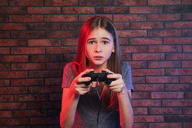 Teenage girl playing video games with controller near brick wall