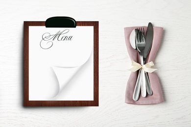 Cutlery set and empty menu on white wooden background, top view