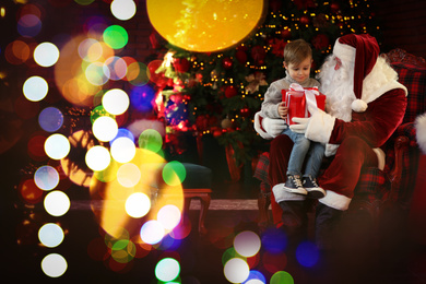 Santa Claus and little boy with gift near Christmas tree indoors