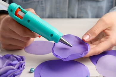 Photo of Woman with hot glue gun making craft at wooden table, closeup