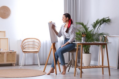 Happy woman artist drawing picture on canvas in studio