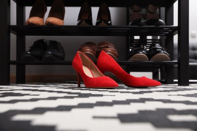 Photo of Stylish red female shoes near shelving unit in hall