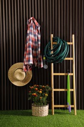 Photo of Beautiful blooming marigolds, gardening tools and accessories on green grass near wood slat wall