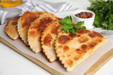 Board with delicious fried chebureki and parsley on white table