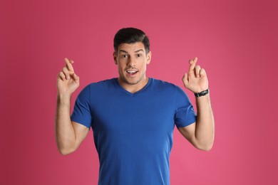 Man with crossed fingers on pink background. Superstition concept