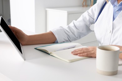 Photo of Doctor with tablet and notebook at desk in clinic, closeup. Online medicine concept