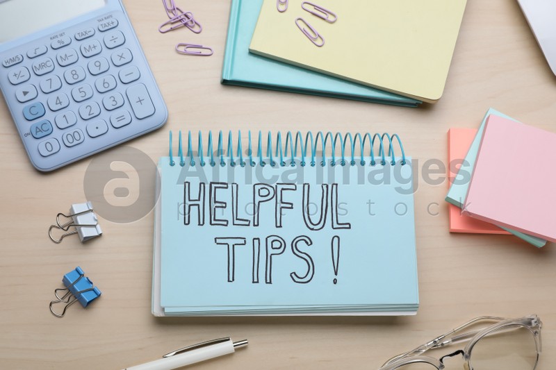 Photo of Notebook with phrase Helpful Tips and stationery on wooden table, flat lay