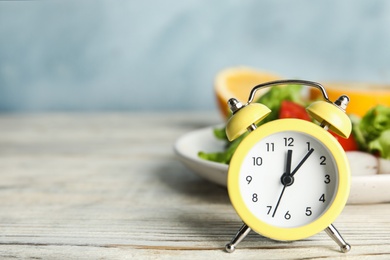 Alarm clock and healthy food on white wooden table, space for text. Meal timing concept