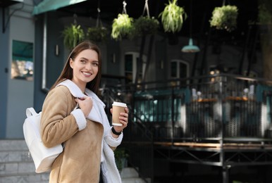 Young woman with stylish white backpack and cup of drink on city street, space for text